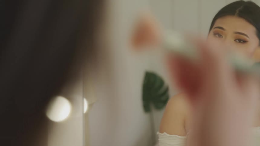 Woman looking in mirror applies makeup with brush