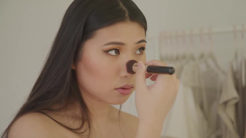 Young woman applies makeup to her face in a changing room