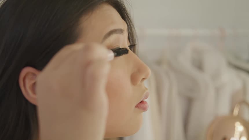 Side view of an asian woman putting on makeup in dressing room