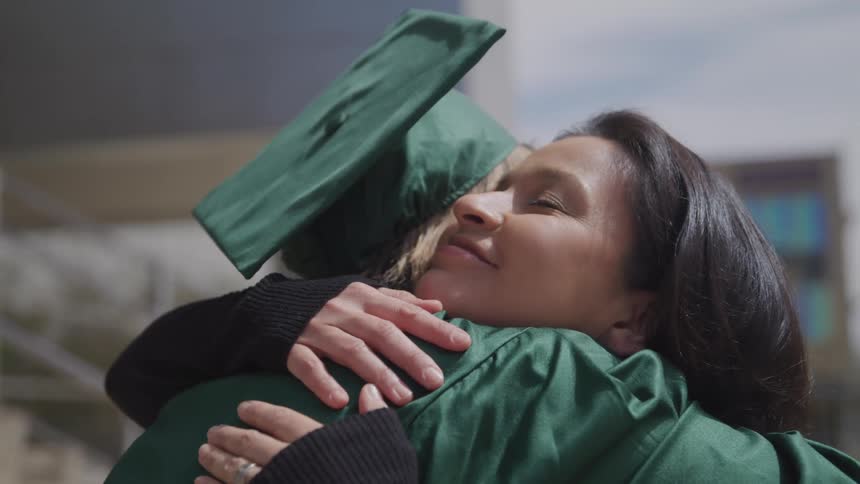 A woman hugs a teenage girl in her graduation cap and gown