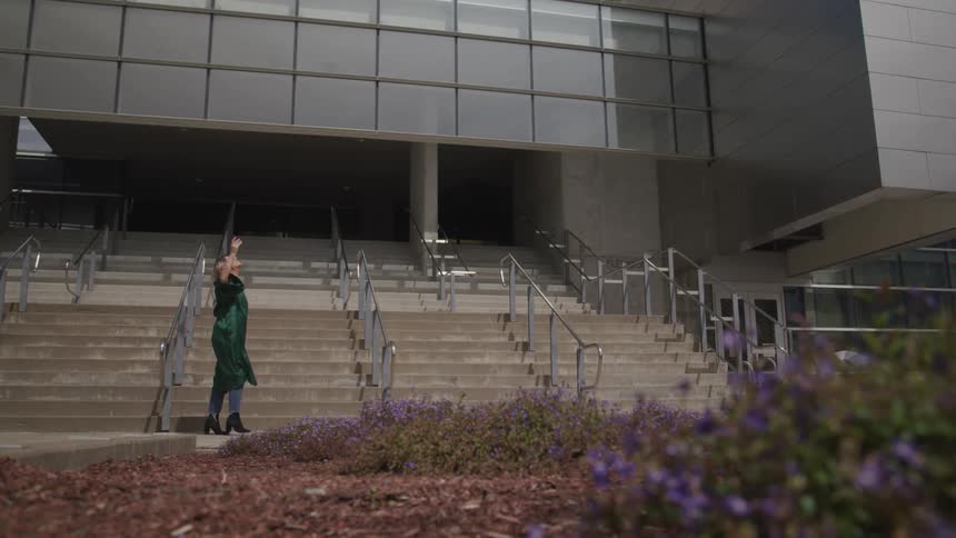 A woman wearing a dark graduation gown throws her cap high into the air