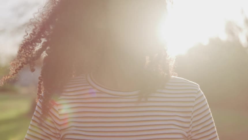 A teenage girl stands outside as the sun shines down on her