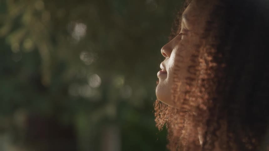 The sun shines on the face of a young woman as she faces the sky while standing outdoors