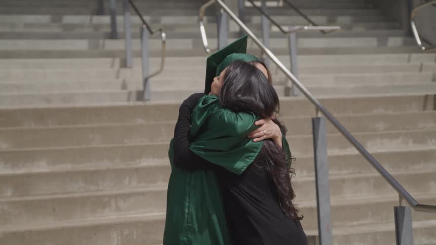 A mother hugs her daughter who is wearing her graduation gown