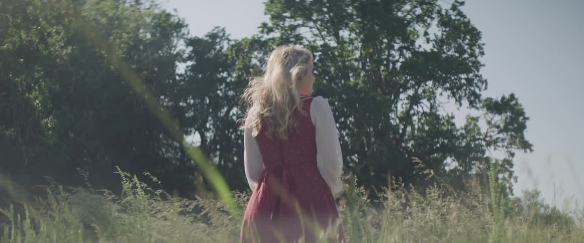 Young woman in prairie style dress stands in tall grass