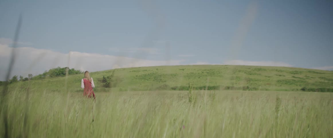 A woman walks through a grassy field on a sunny day