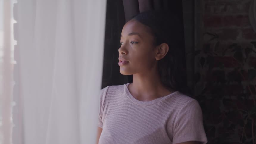 A young black woman looks out of a window contemplatively