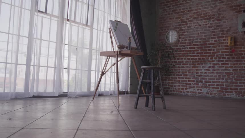 Easel and canvas with a stool in front of a window in a studio