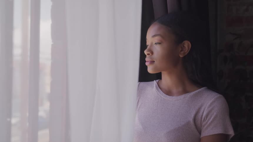 Young black woman stands next to window with curtain