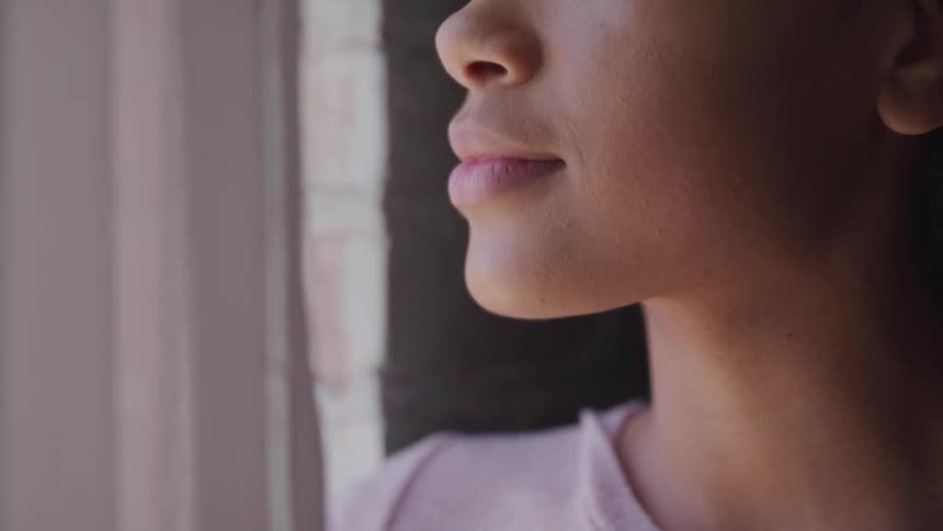A woman standing and staring out of a window with curtains