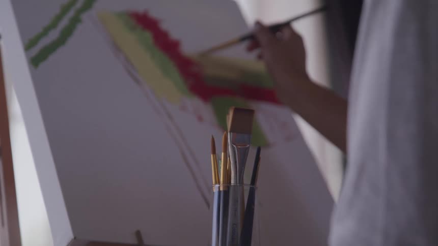 A woman sitting and painting on a canvas with a paintbrush