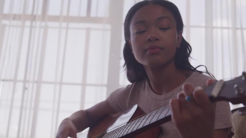 Young woman plays acoustic guitar sitting in a room at home