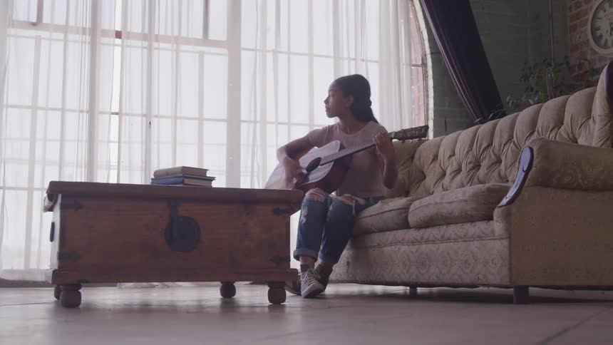 A woman is sitting on a couch and playing guitar