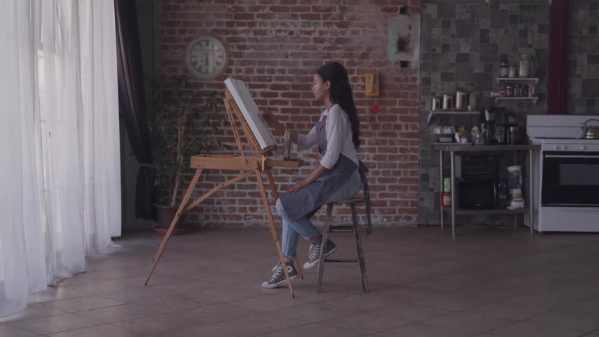 Young woman painting in canvas on an easel at home