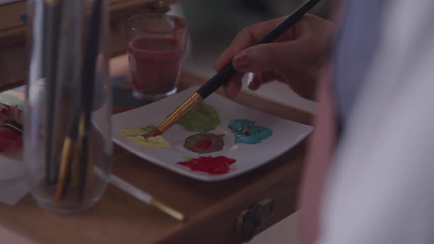 A person dipping a paint brush into paint from a plate