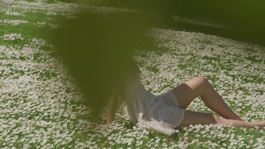 A woman in a white mini dress sunbathes in a field of white flowers