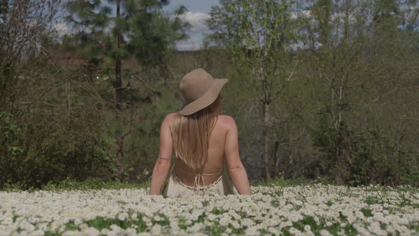 Young woman wearing a dress and sun hat sitting on a field of white wild flowers