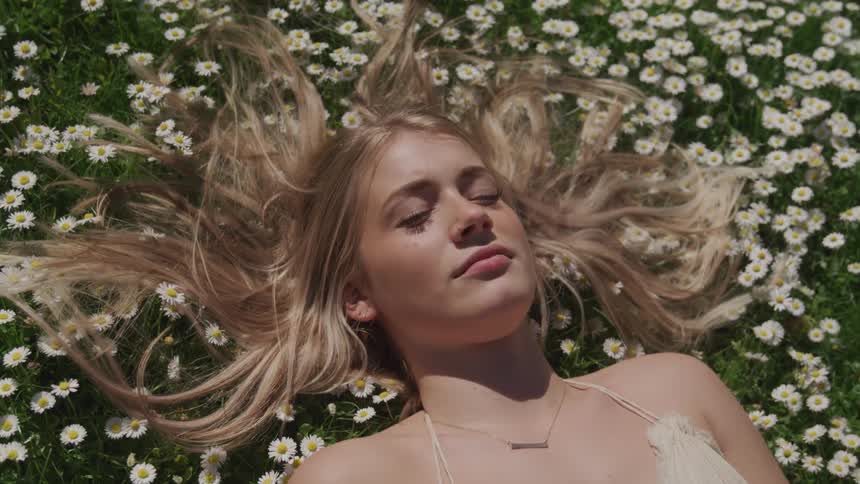 A young woman rests on her back among flowers in a field on a sunny day