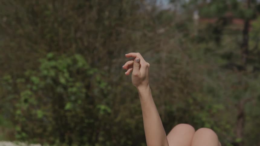 Person sitting outside in wilderness reaches up with one hand