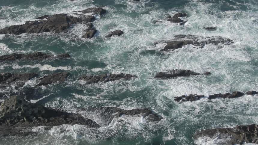 Oceans waves crash around scattered rock formations on the ocean during the day