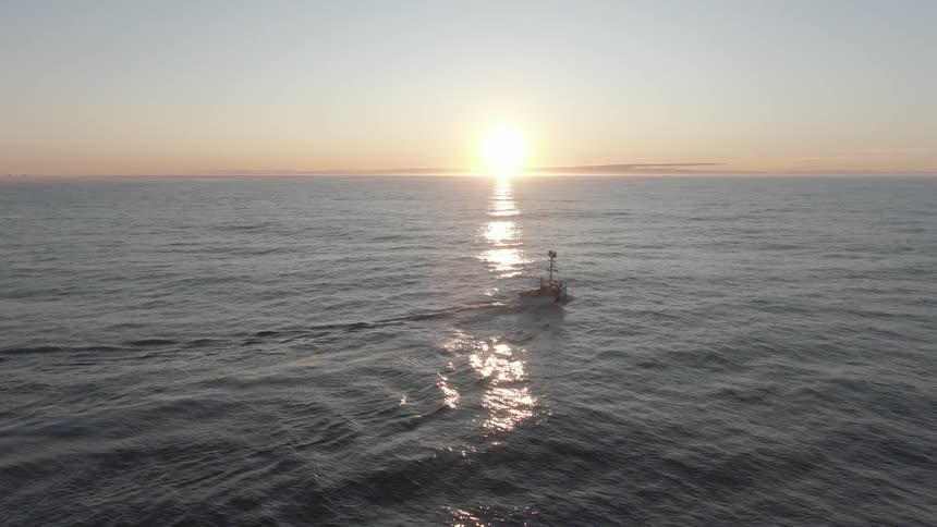 A boat floating in the ocean water with the sky clouds and a sunset in the background