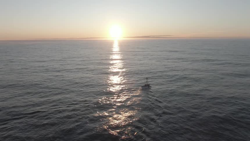 A boat sailing in the ocean as the sun sets