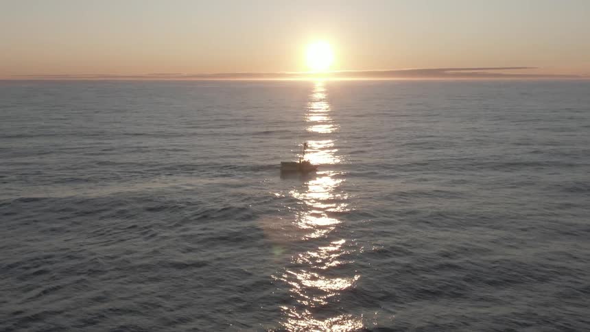 An aerial view of a boat in the ocean as the sun sets