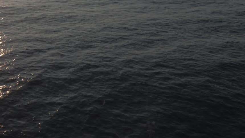 A boat travels over the ocean towards the horizon at sunset