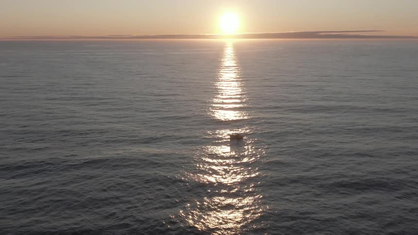 A boat bobs in the ocean as the rising sun shines on the surface of the water
