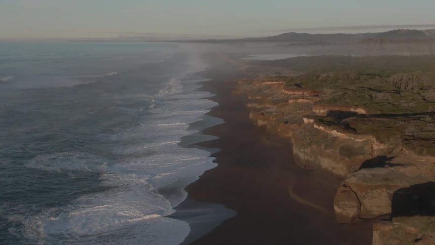 Aerial view of ocean waves breaking against the shoreline with cliffs