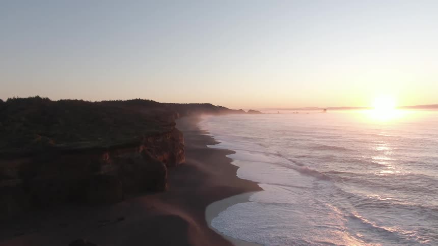 A beach with sand and waves with the sky and a sunset in the background