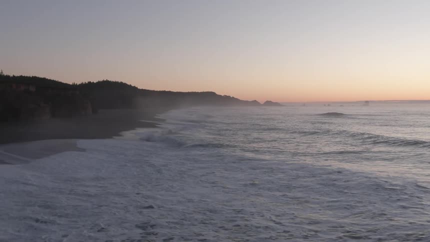 Aerial view of high tide waves on the coast of a beach at sunset