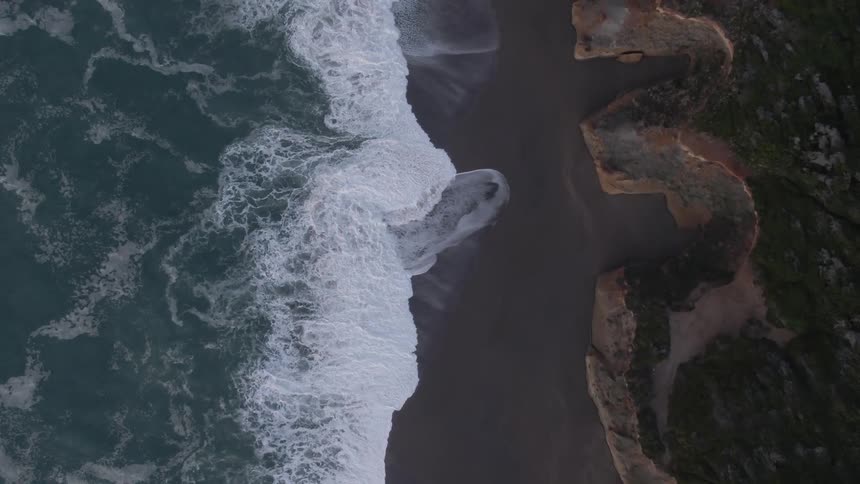 Surf flows up black sand beach nearing but not reaching cliffs