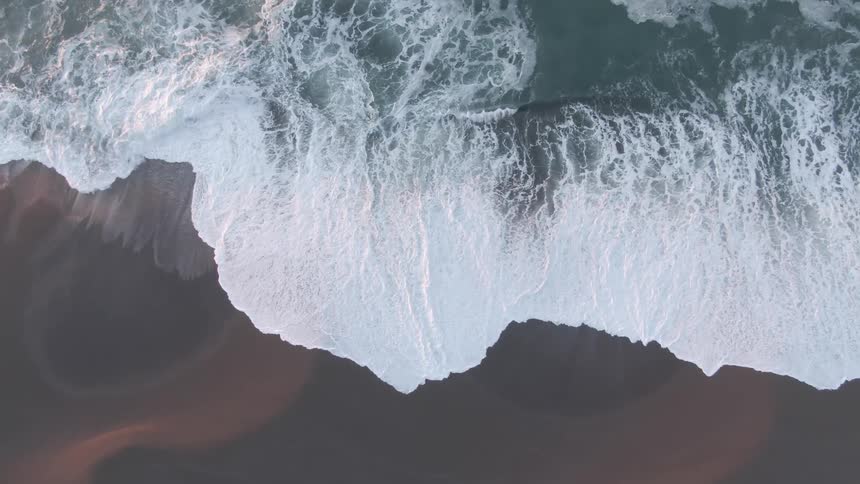 Aerial view of foamy ocean waves breaking against wet beach sand