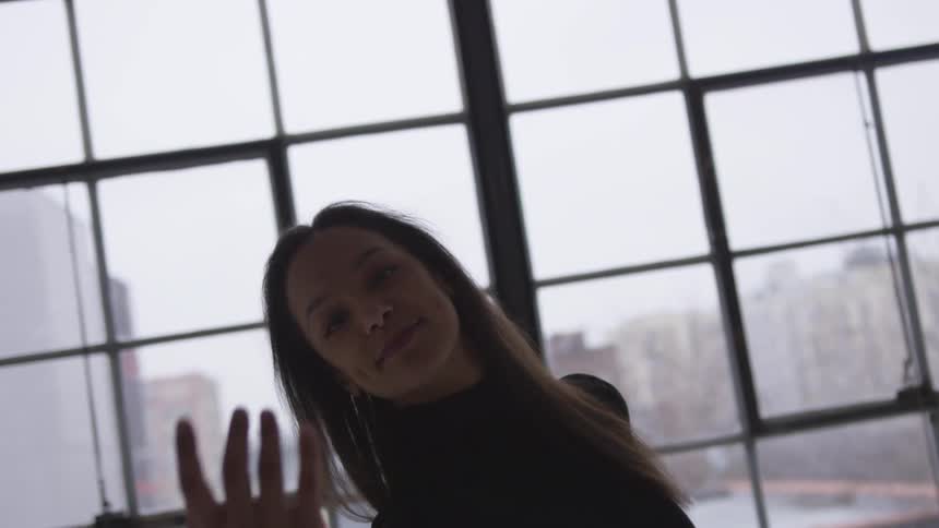 A ballet dancer practices in a studio in front of a large window with views of downtown