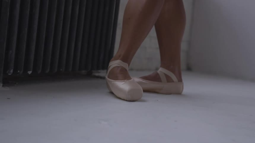 A dancer wearing pointe shoes takes a ballet pose near a radiator