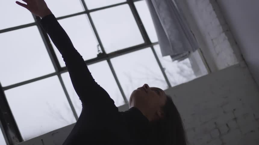 A woman is doing a dance pose in doors next to a window