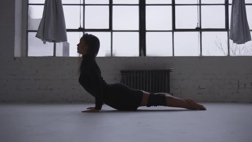 Young flexible woman in a black dress stretches on the floor of a studio