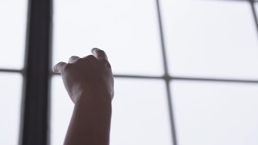 A woman holding up her hand with a window the sky and clouds in the background