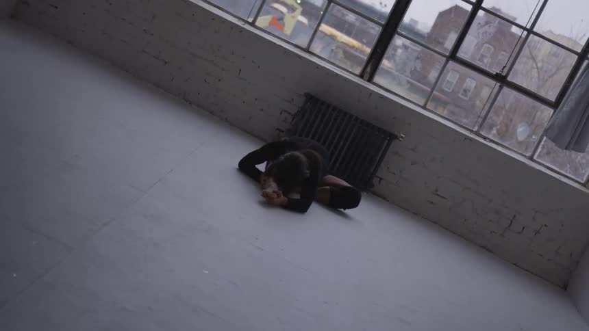 Young woman in a black dress lays on the white floor of a studio in the city