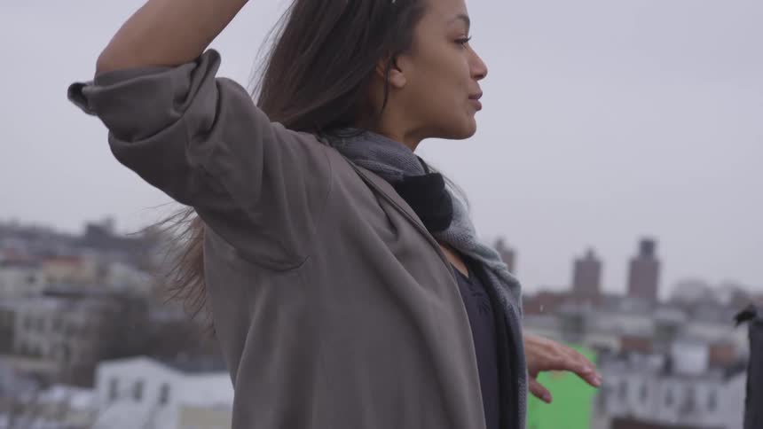 A young female dancer dances atop a rooftop as snow falls from the sky around her