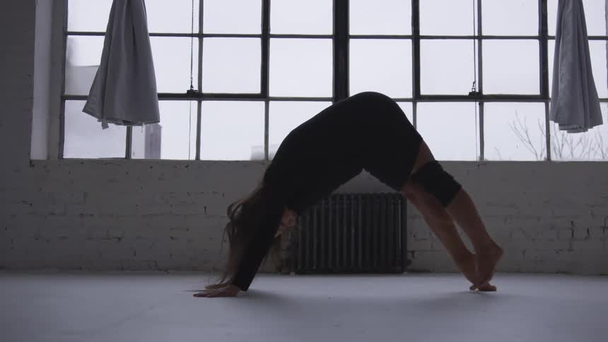 Woman performs yoga near window showing buildings and leafless trees