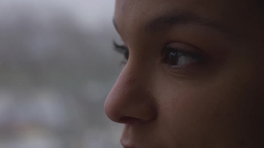 A woman staring off into the distance and blinking with a window and the sky in the background