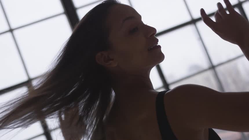 A female dancer spins while dancing in front a set of large windows