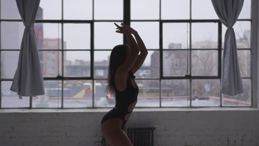 A young female ballerina dances in front of a large window in a building in a metropolis during the day