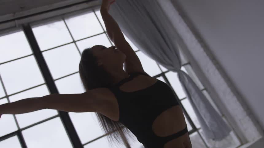 Young woman in leotard poses in front of large window