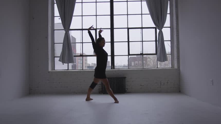 A woman is dancing in a room next to a window
