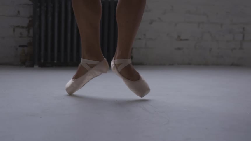 A womens feet with ballerina shoes in a room dancing with a wall and a radiator in the background