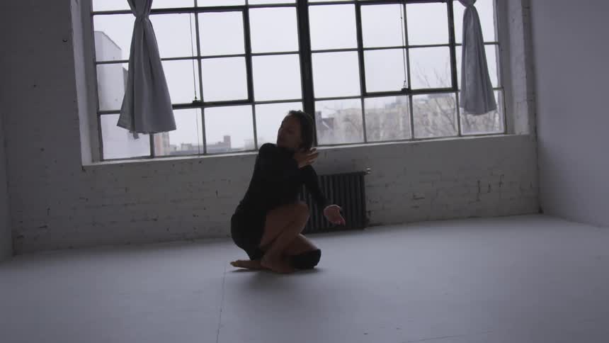 A woman in a black dress dancing in a room with a window in the background