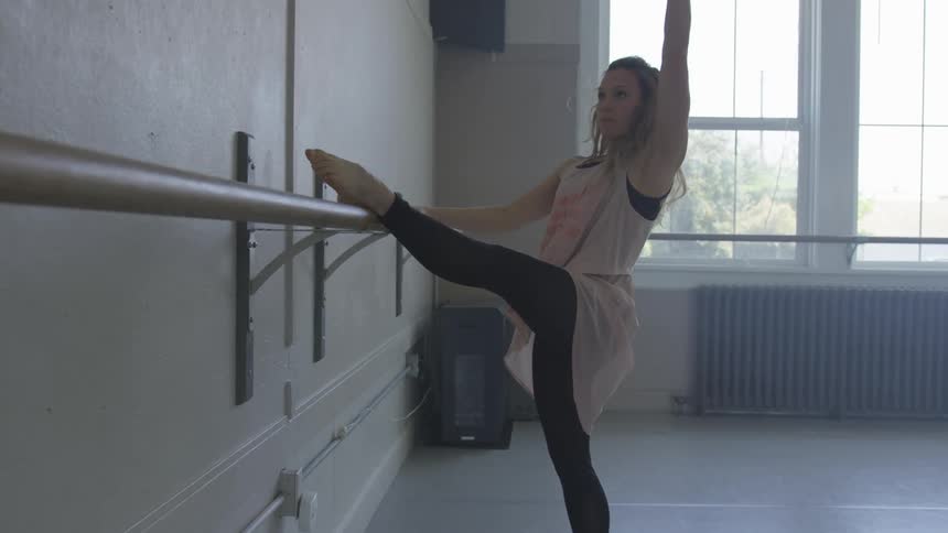 A woman in a dance studio stretching with a radiator and a window in the background